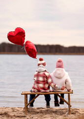 young couple sitting on bench on the beach with two red balloons