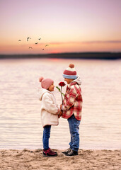 romantic kids couple standing on the beach in sunset light and holding a red rose 