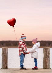 boy and girl holding hands and a red balloon on wooden pier near the sea