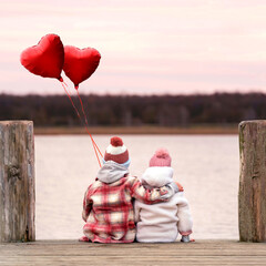 cute children sitting together on the wooden pier, holding red balloons in sunset light