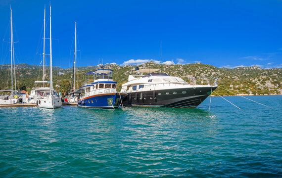 Panoramic wooden pier walkway lined with traditional Turkish gulets and boats flying red flags in a turquoise marina bay. Serene summer scene with green hills and blue skies,