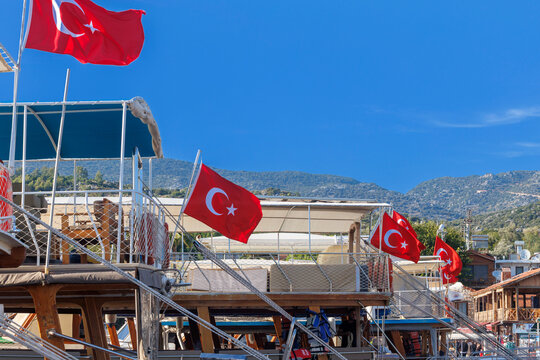 Panoramic wooden pier walkway lined with traditional Turkish gulets and boats flying red flags in a turquoise marina bay. Serene summer scene with green hills and blue skies,