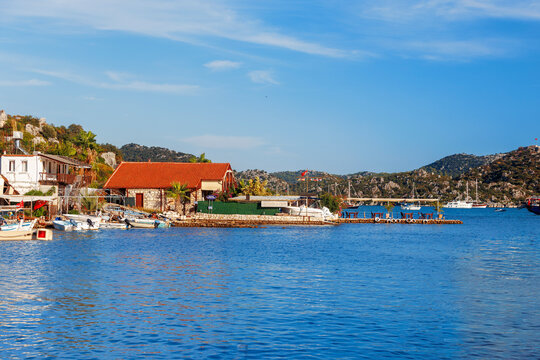 Panoramic wooden pier walkway lined with traditional Turkish gulets and boats flying red flags in a turquoise marina bay. Serene summer scene with green hills and blue skies,