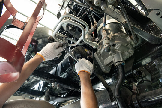 Mechanic hands inspecting and repairing the chassis and undercarriage of a heavy truck 
Close-up of a professional technician in uniform working under a vehicle. Examining the air tank system,