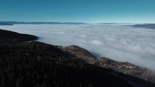 Aerial view of dense clouds covering valleys with snowy mountain ridges rising above the fog, creating a dramatic winter landscape near Sarajevo with clear sky and natural contrast