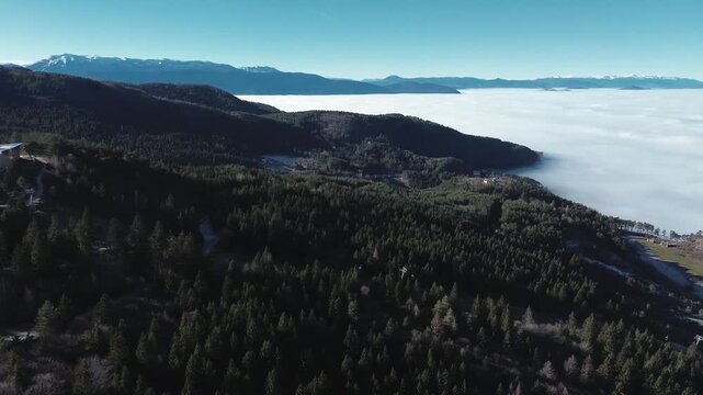 Panoramic aerial view of dense clouds covering valleys with snowy mountain ridges rising above the fog, creating a dramatic winter landscape near Sarajevo with clear sky and natural contrast