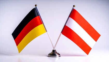 Crossed flags of Austria and Germany on small poles against neutral background, symbolizing European unity and heritage.