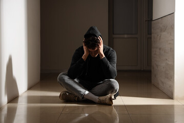 Sad young man sitting on floor in hall. International Stress Awareness Week