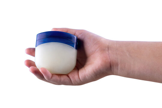 Hand holding a small jar of petroleum jelly, isolated on a black background