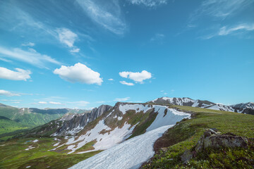Scenic view from grassy flowering cliff along ridge with snow cornice to sharp rocks and rocky...