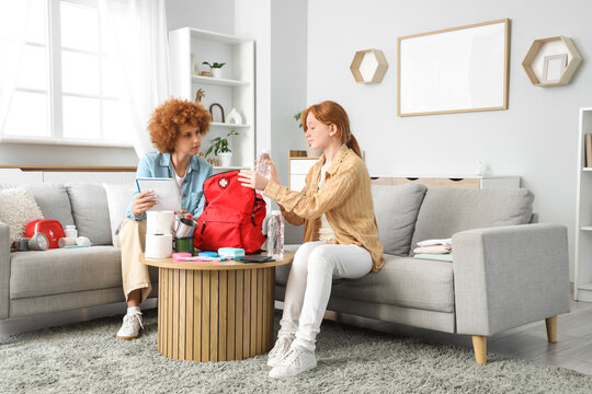 Redhead mother with check-list and her teenage daughter packing emergency backpack at home - Powered by Adobe