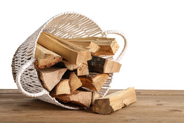 Wicker basket with firewood logs on wooden table against white background © Pixel-Shot