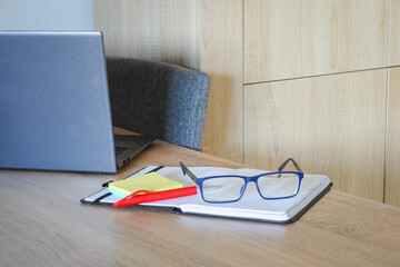 Eyeglasses and notebook on wooden desk with laptop in modern workspace