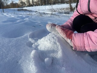 A girl in gloves sculpts from white fluffy snow in a winter park