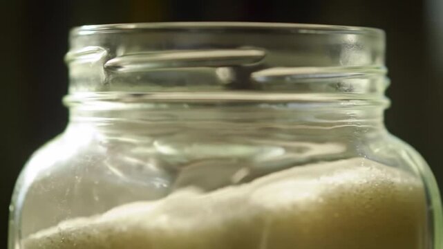 Close up of a glass jar with light colored contents against a dark backdrop