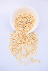 Puffed Rice Spill From White Bowl on Light Background, Breakfast Snack, And Cooking Concept. Puffed rice tumbles from a white bowl onto a pale surface.