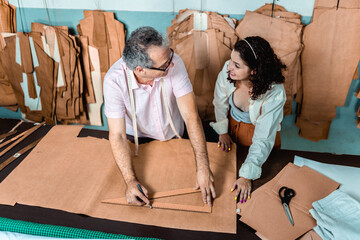 Professional tailor and apprentice working together on clothing patterns in a fashion atelier workshop.