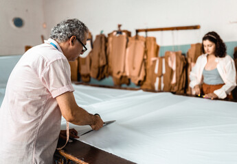 Professional male tailor cutting light blue fabric with scissors in a garment workshop with an...