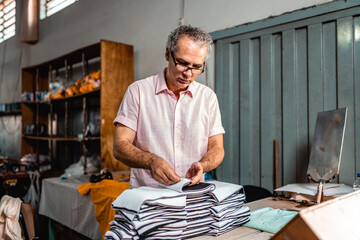 Experienced male worker inspecting and folding striped fabric pieces in a textile manufacturing...