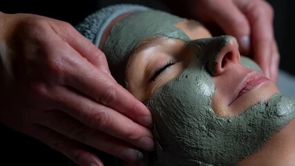 Aesthetician gently spreading a thick mud mask on a clients face in a serene spa setting for deep skin cleansing and relaxation.