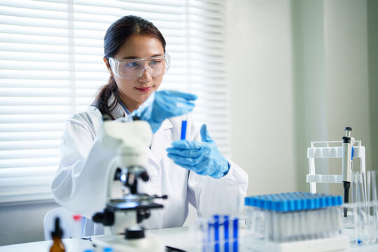 Asian adult female scientist researcher conducts experiment holds test tube chemical analysis professionally carefully with focus modern laboratory medical science facility