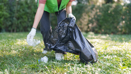 Adult volunteer hand picking plastic bottle litter from green grass promoting environmental sustainability conservation efforts
