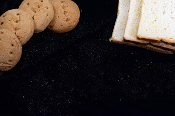 A rustic arrangement shows round cookies beside slices of white bread on a dark background.