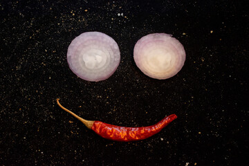 Smiling Face Made From Onion Slices And Red Chili Pepper On Dark Kitchen Surface