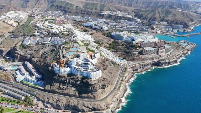 The Terraced Paradise: 4K Aerial of People Relaxing at Luxury Cliffside Resorts Overlooking Puerto Rico Marina and the Atlantic Coastline, Gran Canaria, Spain