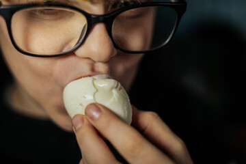 Young boy with glasses is holding a cracked egg close to his mouth, showcasing curiosity and...