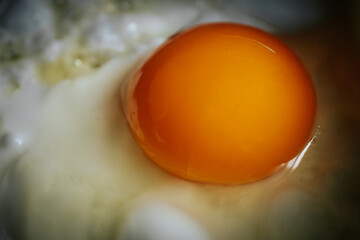 Close-up of a vibrant orange egg yolk nestled in a pool of creamy egg white, showcasing the rich...