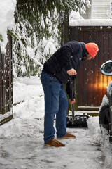 Man clearing snow near a car in winter yard, using a snow shovel during snowfall. Outdoor seasonal work, cold weather, driveway cleaning and winter home maintenance