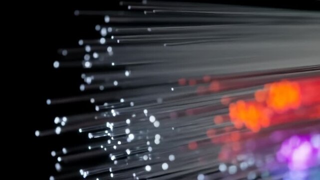Close-up of glowing fiber optic strands transmitting colorful light signals in the dark.
