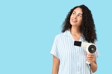 Beautiful young African-American woman with modern hair dryer on blue background