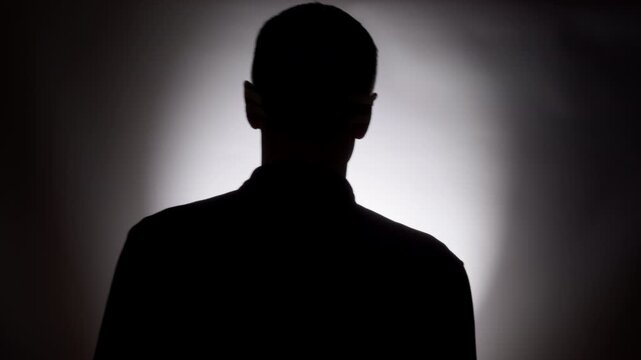 A silhouette of a man walking toward the light in a dark room. Concept of loneliness and mystery.