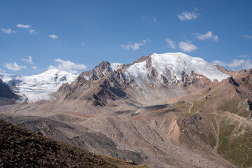 Winding gravel road in the high mountains of Tien Shan with a view of the massive Tuyuksu glacier. Remote alpine landscape in Central Asia