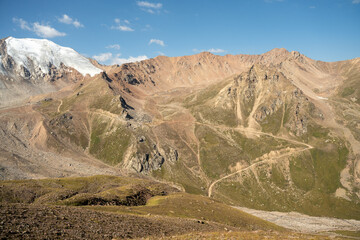Winding gravel road in the high mountains of Tien Shan with a view of the massive Tuyuksu glacier. Remote alpine landscape in Central Asia