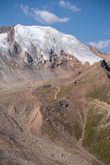 Winding gravel road in the high mountains of Tien Shan with a view of the massive Tuyuksu glacier. Remote alpine landscape in Central Asia
