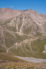 Winding gravel road in the high mountains of Tien Shan with a view of the massive Tuyuksu glacier. Remote alpine landscape in Central Asia