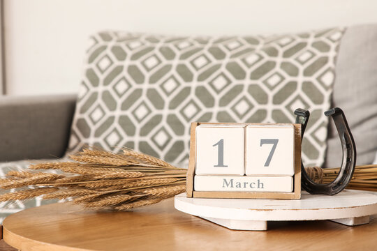 Cube calendar with date of St. Patrick's Day, horseshoe and spikelets on table in living room, closeup