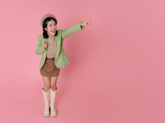 Promotion direction portrait excited Asian woman pointing forward opportunity concept marketing call to action energetic gesture fashion lifestyle style pink studio background with copy space.