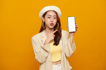 Fashion lifestyle promotion portrait of smiling Asian woman holding smartphone mockup with blank screen presenting mobile application modern digital marketing yellow studio background.