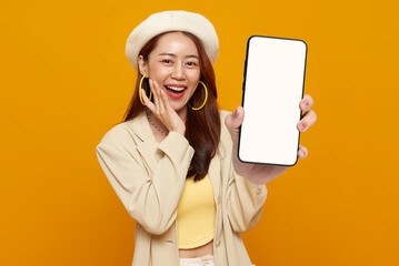 Fashion lifestyle promotion portrait of smiling Asian woman holding smartphone mockup with blank screen presenting mobile application modern digital marketing yellow studio background.