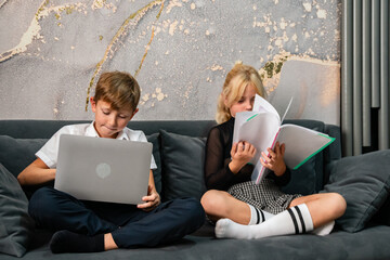 Kids Laptop Homework Couch: Two children study on a couch, one using a laptop, the other reading a book.