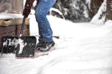 Man shoveling snow in a backyard during winter, clearing a path near a house. Snowy weather, warm clothing, seasonal outdoor work and home maintenance in cold climate