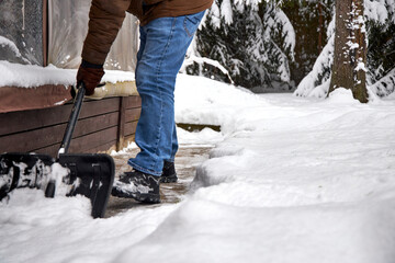 Man shoveling snow in a backyard during winter, clearing a path near a house. Snowy weather, warm clothing, seasonal outdoor work and home maintenance in cold climate