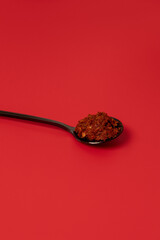 Homemade spicy chili sauce in black teaspoon on red