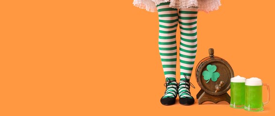 Female legs in striped stockings, barrel and mugs of beer on orange background with space for text. St. Patrick's Day celebration