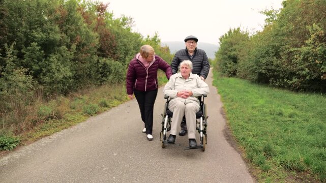 Group of elderly friends with grey hair and walker and wheelchair take a walk in the park talking and having fun enjoying nature
