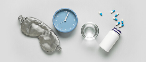 Melatonin pills with glass of water, alarm clock and sleeping mask on grey background